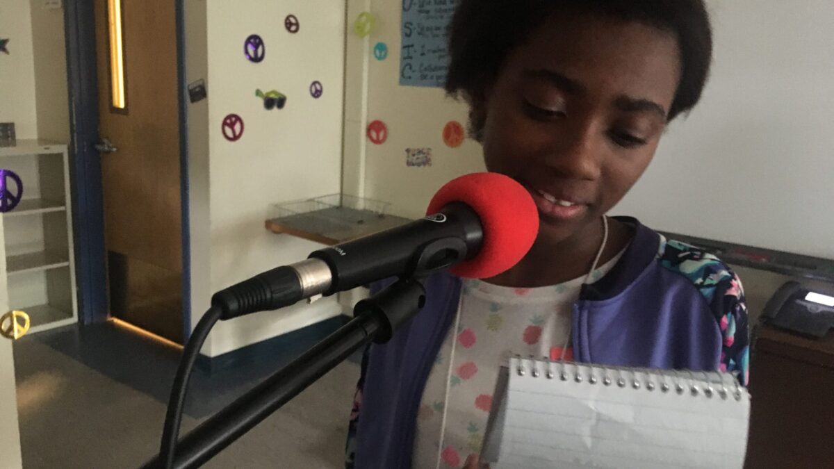 Youth reading from a notepad and speaking into a microphone in a classroom