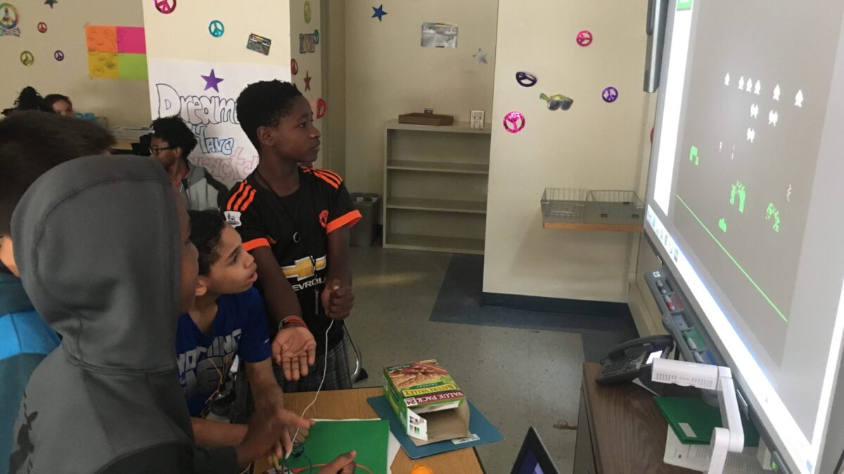 Three youth playing an old school arcade game on a projected screen