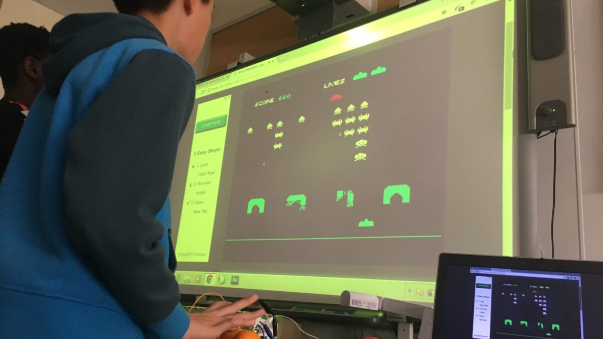 A youth playing an old school arcade game on a projected screen, using oranges as the controller