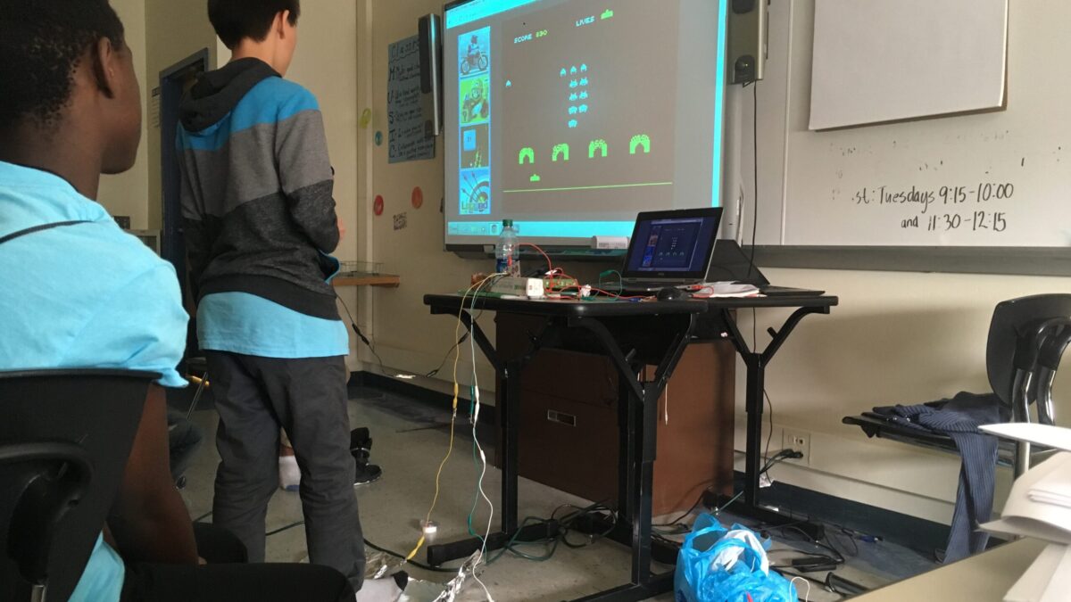 A youth playing an old school arcade game on a projected screen as another youth watches