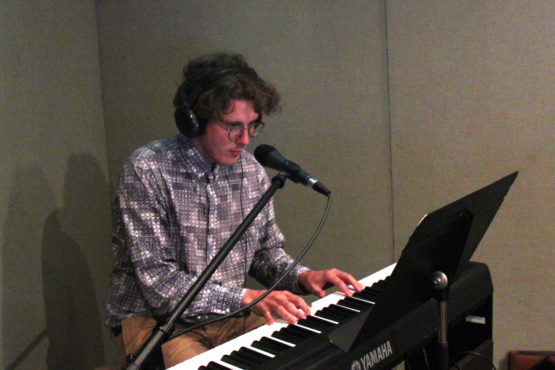 Adult wearing headphones playing a piano keyboard in a radio studio