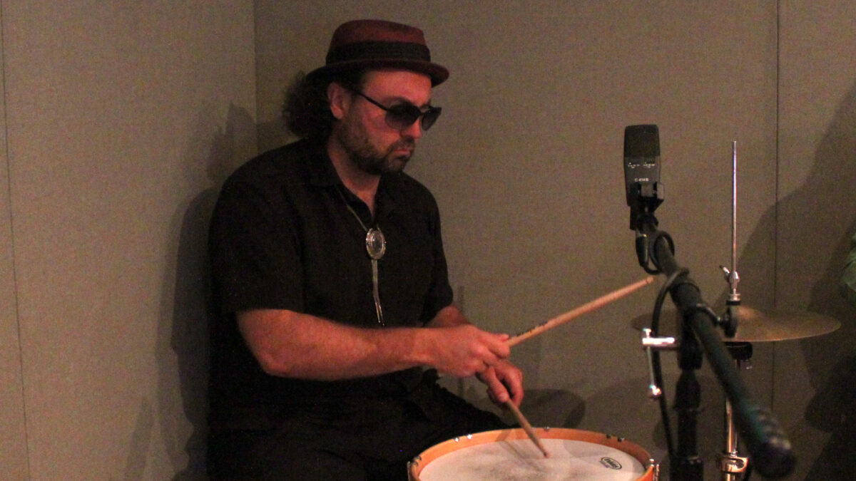 An adult playing drum set in a radio studio