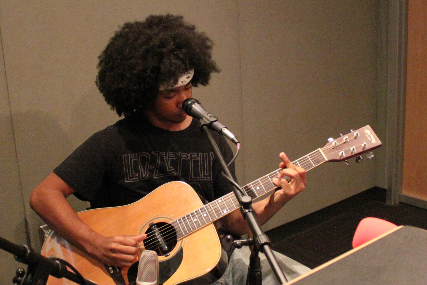 Teen playing acoustic guitar into a microphone in a radio studio