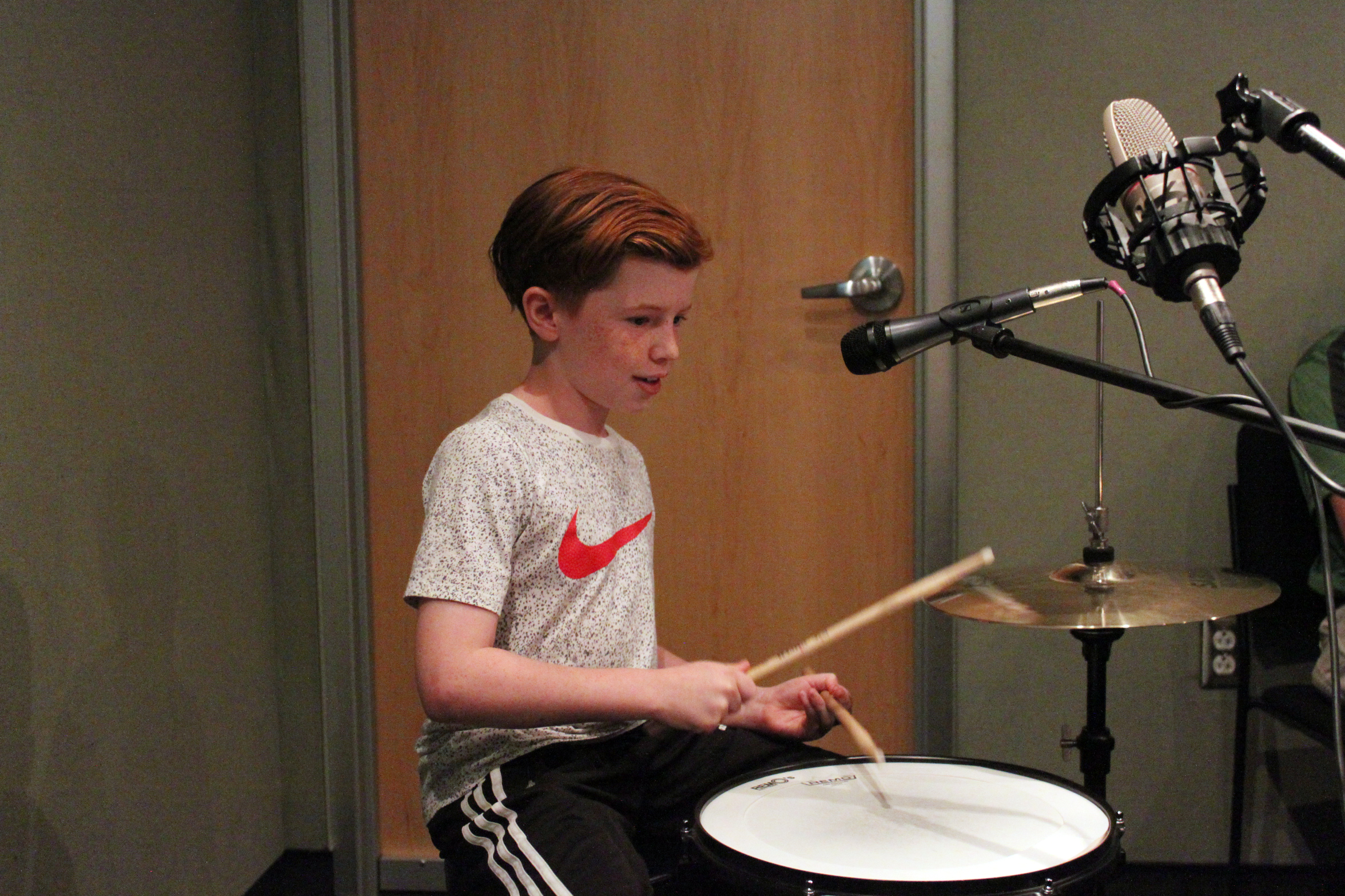 A youth playing a drum set in a radio studio