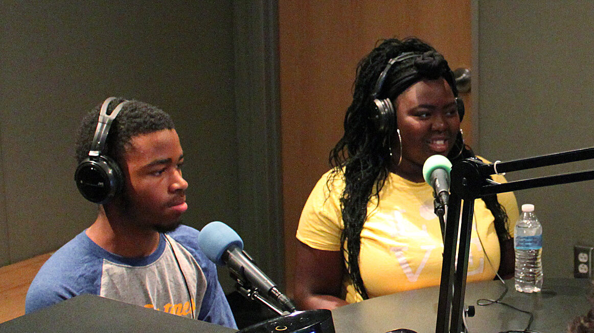 Two teens wearing headphones speaking into microphones in a radio studio