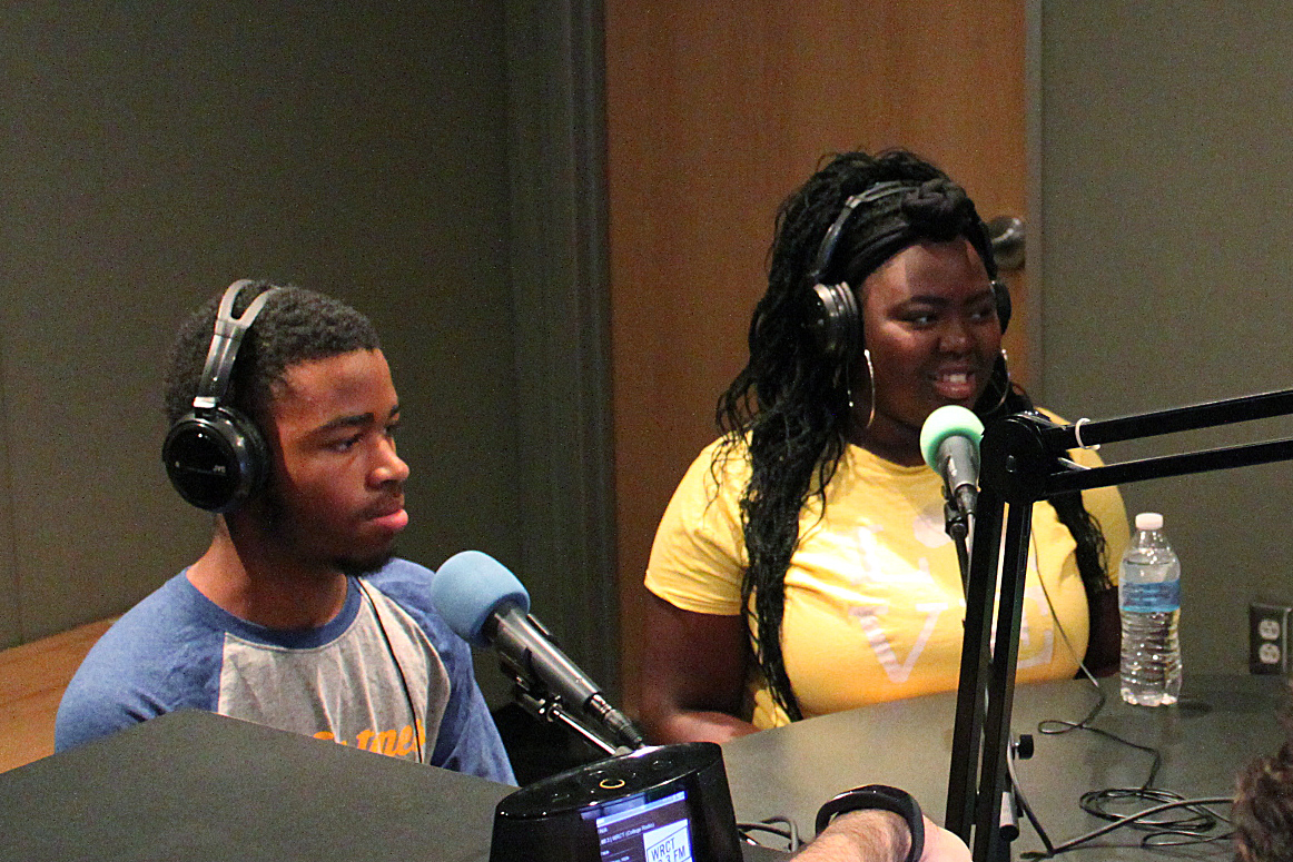 Two teens wearing headphones speaking into microphones in a radio studio