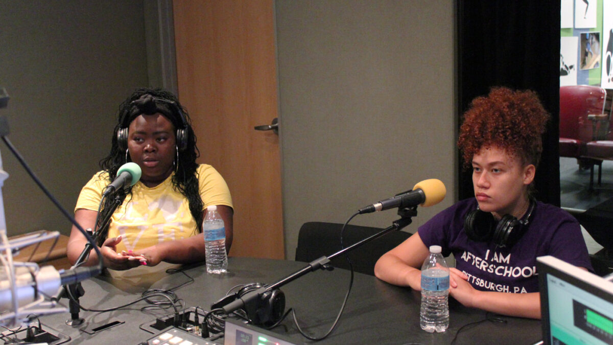 Two teens wearing headphones speaking into microphones in a radio studio
