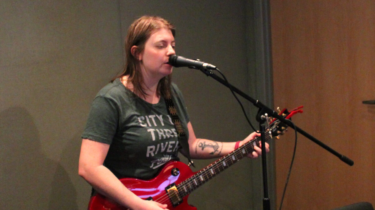 An adult playing electric guitar and singing into a microphone in a radio studio