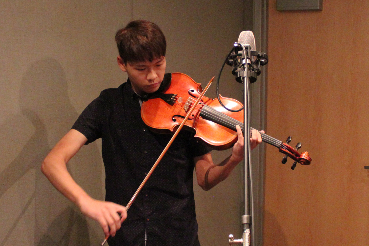 Teen playing violin into a microphone in a radio studio