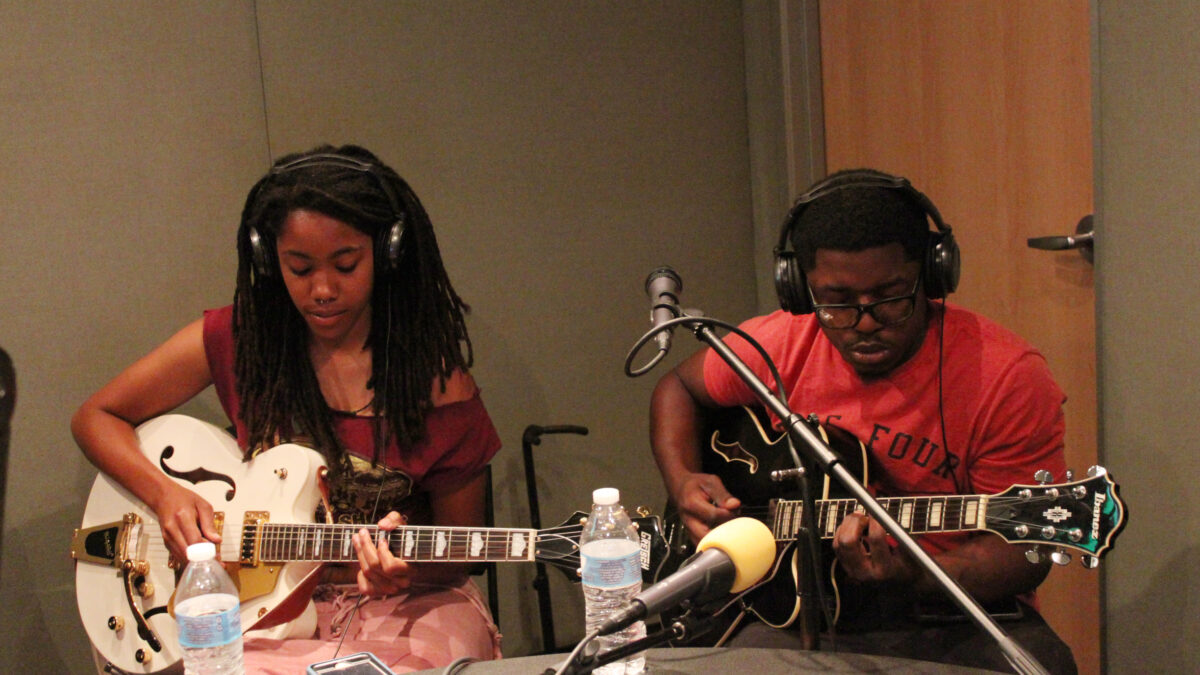 Two teens wearing headphones playing electric guitar in a radio studio