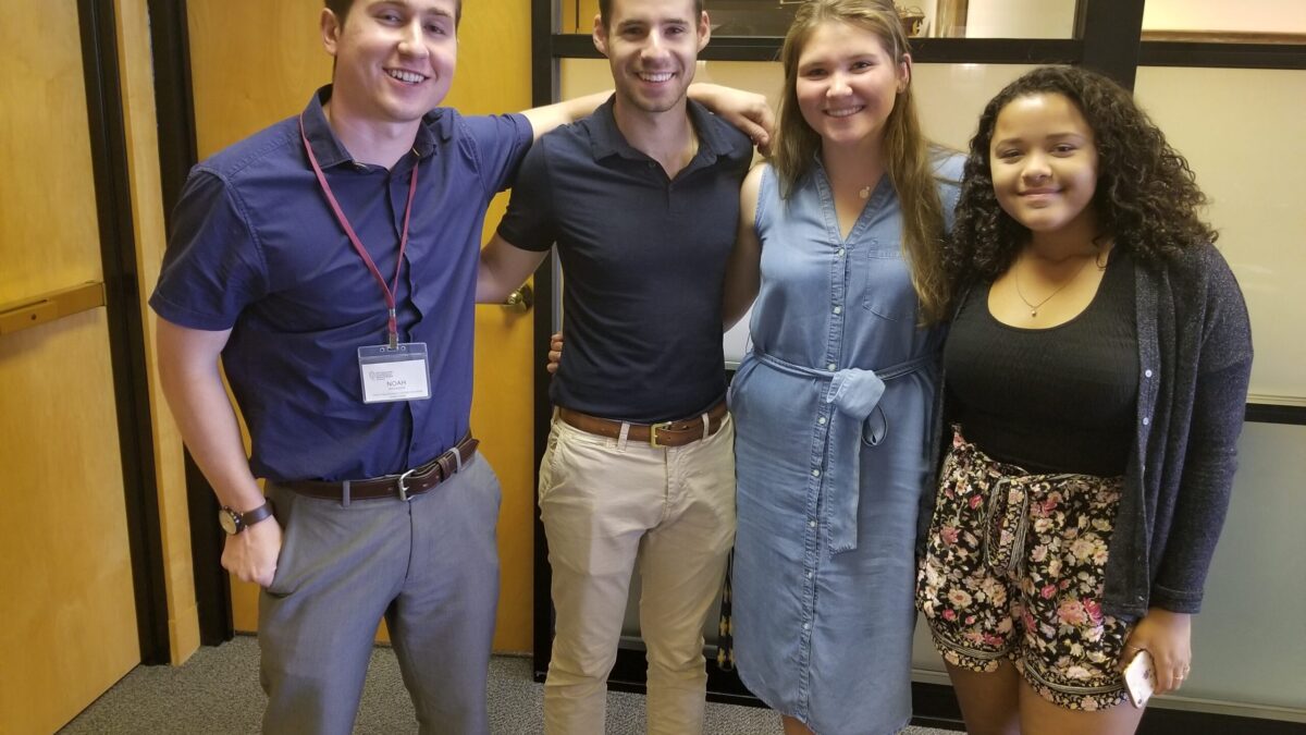 Four teens smiling and posing in profile in an office space