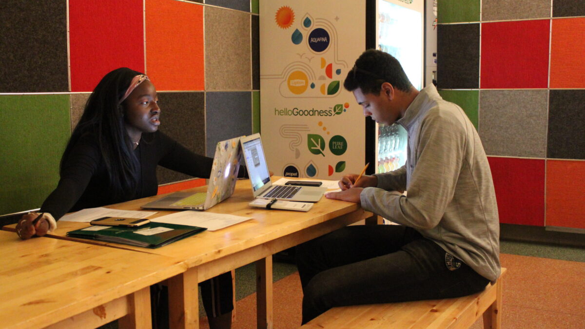 Two teens sitting in front of laptops on a wooden table