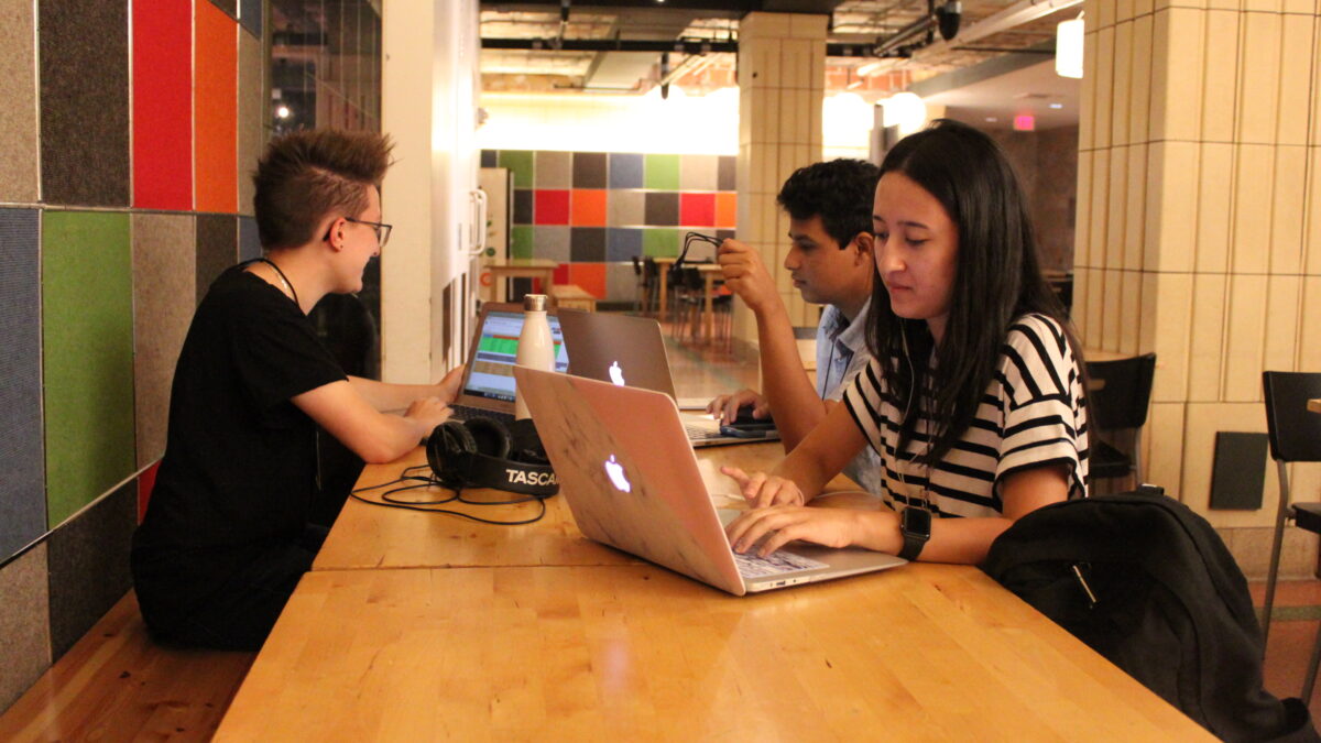 Three teens looking at laptops on a wooden table