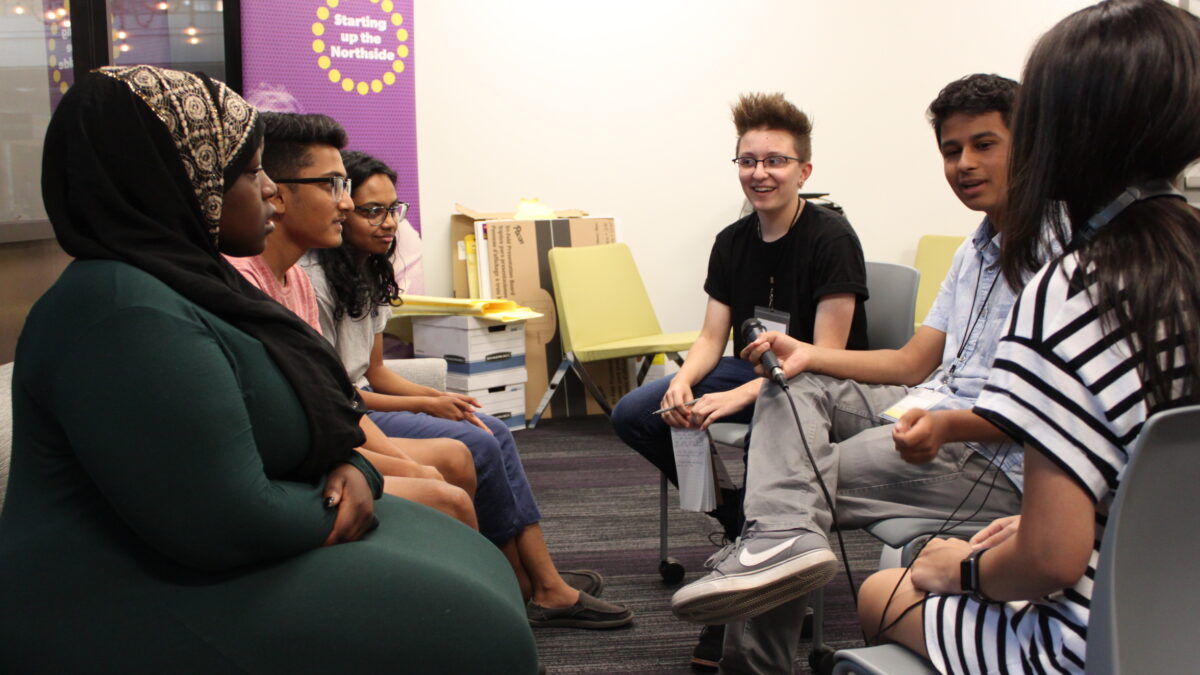 Six teens sitting and having a discussion, one holding a microphone