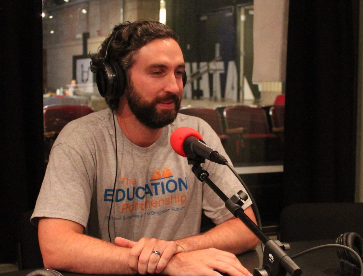 Adult wearing headphones speaking into a microphone in a radio studio
