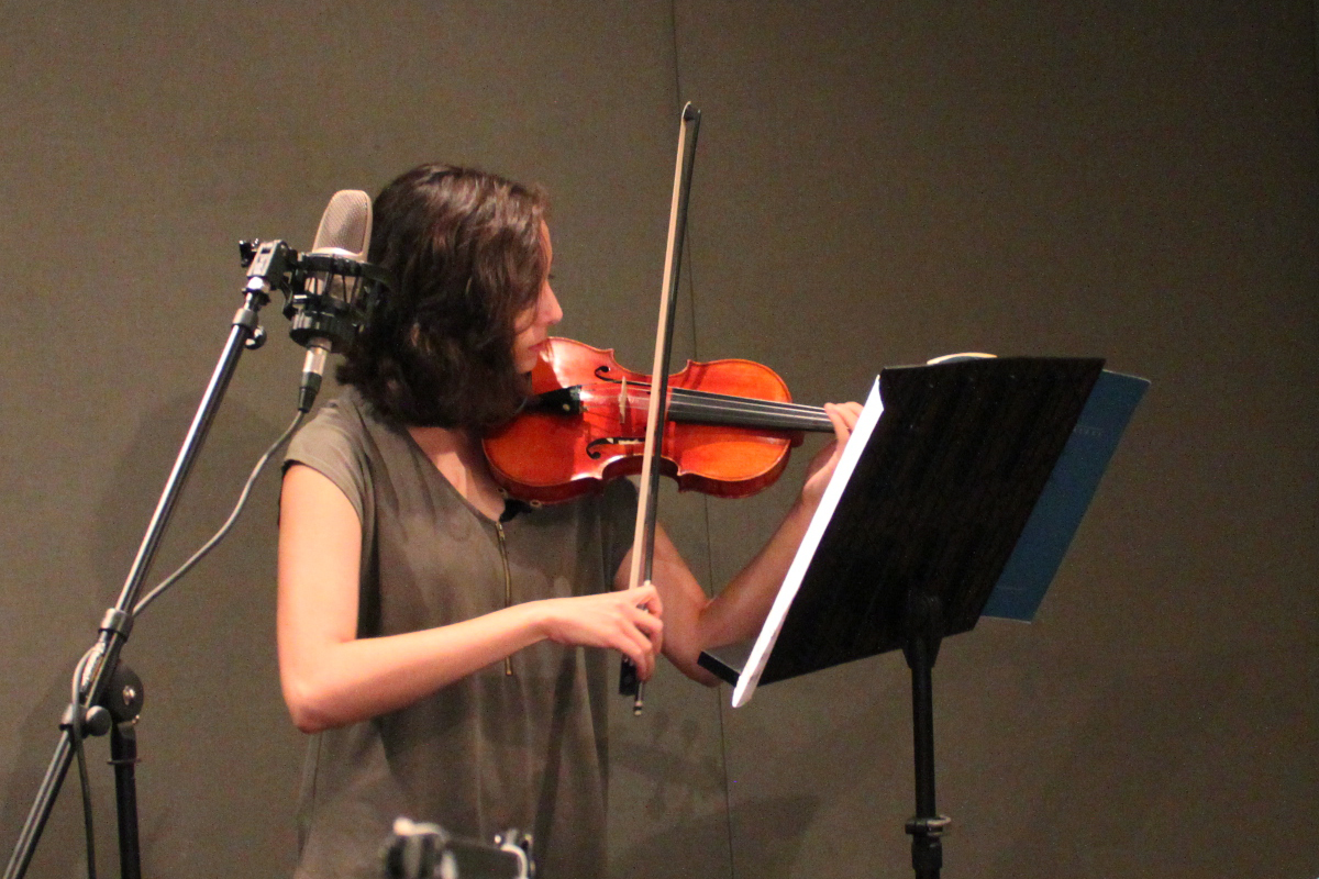 Teen playing violin looking at sheet music on a music stand in a radio studio