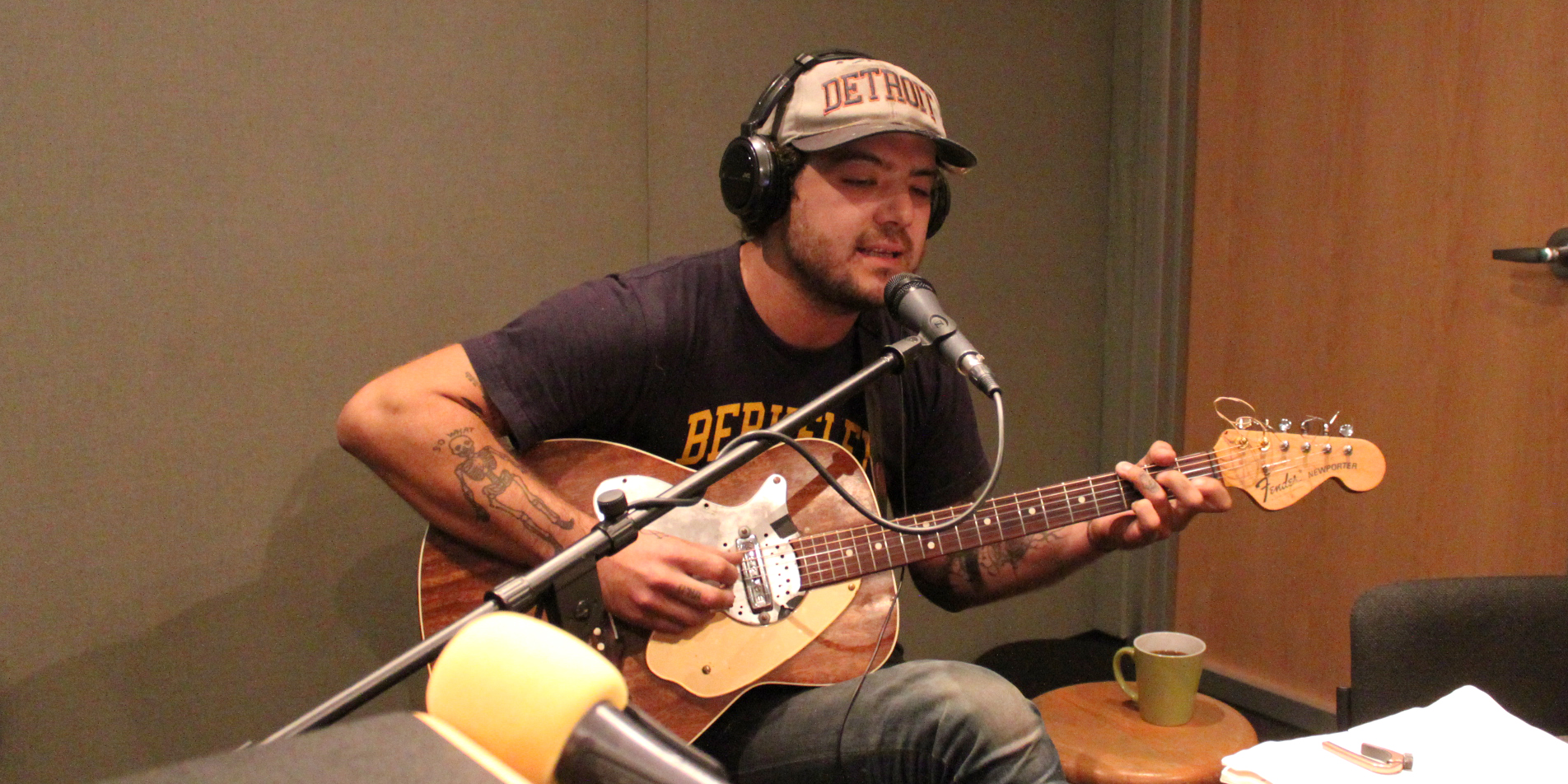 An adult playing acoustic guitar and singing into a microphone in a radio studio