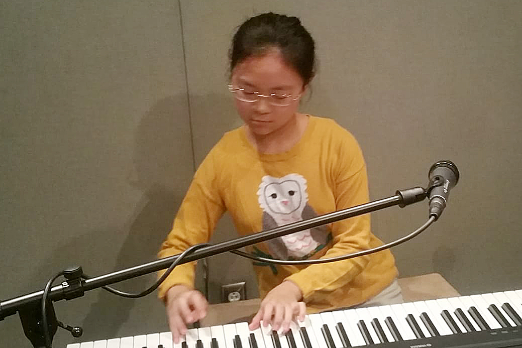 Youth playing piano keyboard behind a microphone