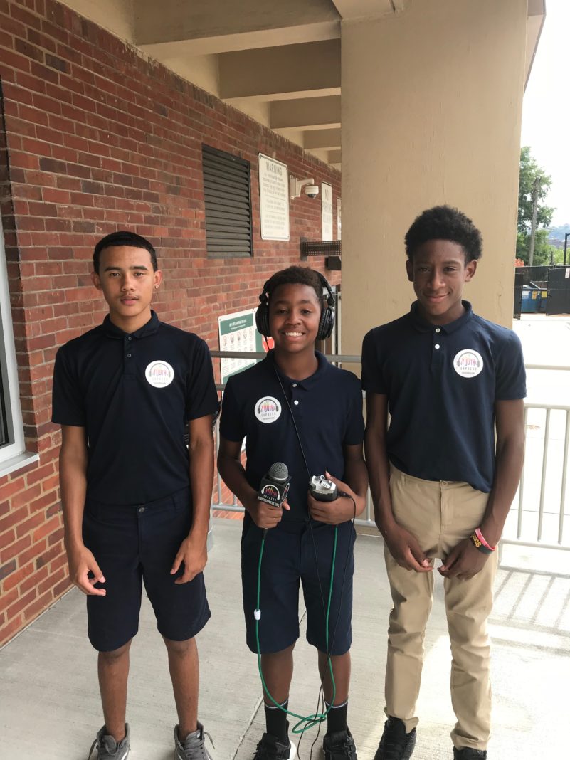 Three teens smiling and posing in profile, one wearing headphones and holding a microphone and a portable recorder