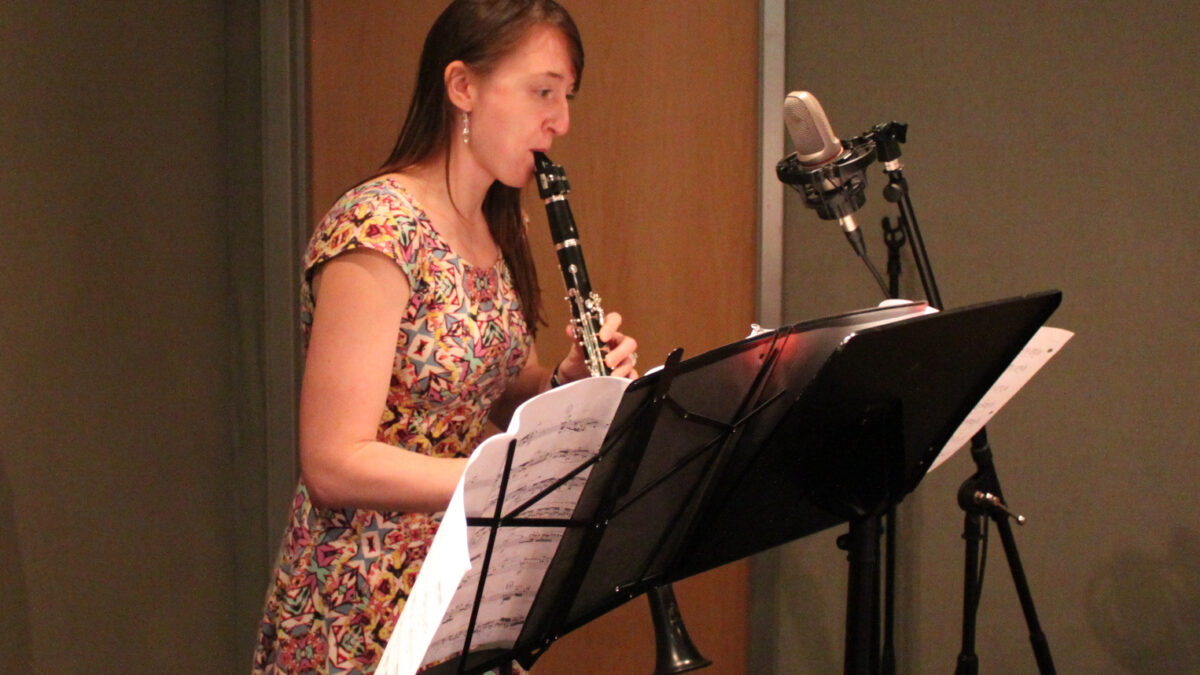 Individual playing clarinet looking at sheet music on a music stand in a radio studio