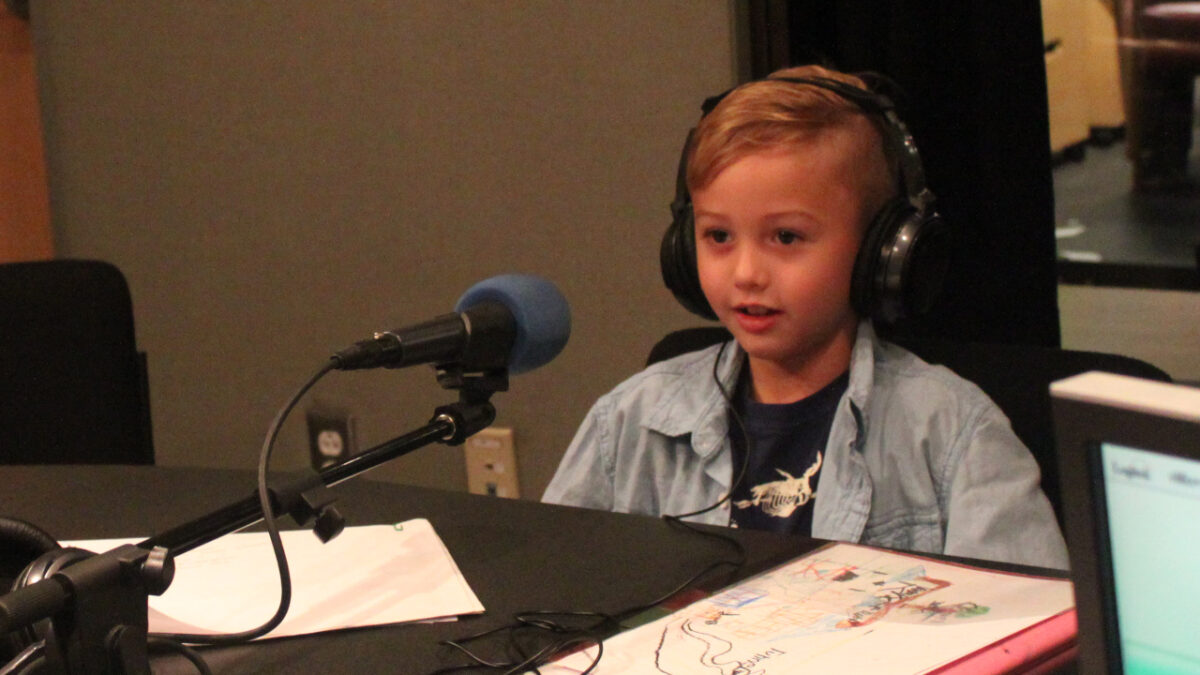 Child wearing headphones speaking into a microphone in a radio studio