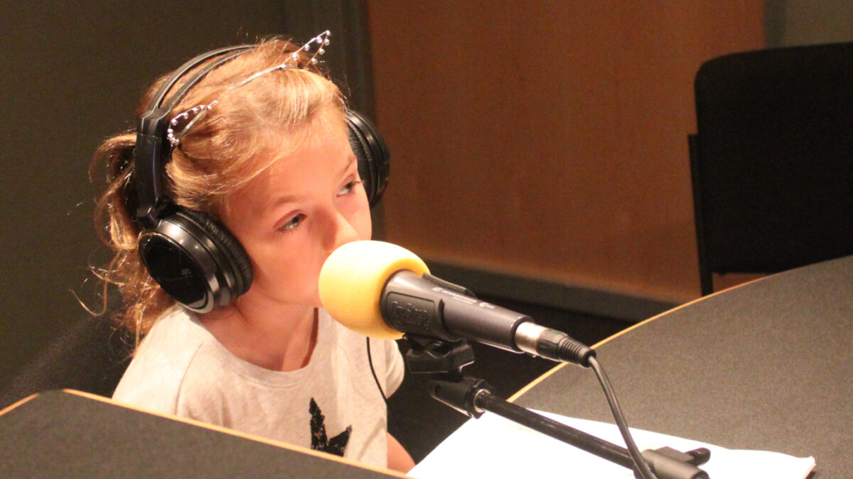 Child wearing headphones speaking into a microphone in a radio studio