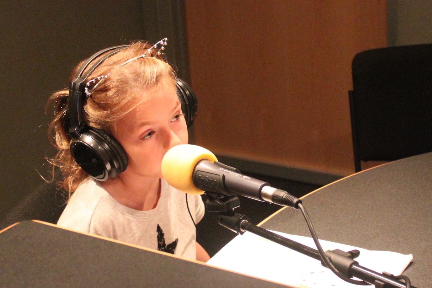 Child wearing headphones speaking into a microphone in a radio studio