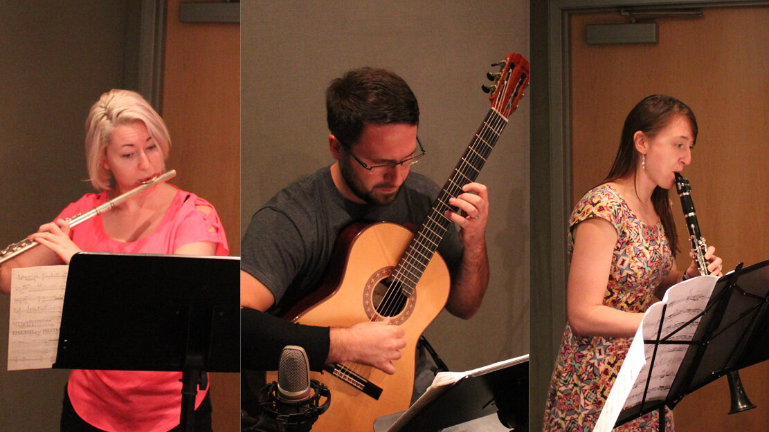 An adult playing flute, an adult playing acoustic guitar, and an adult playing clarinet, all looking at sheet music on music stands in a radio studio