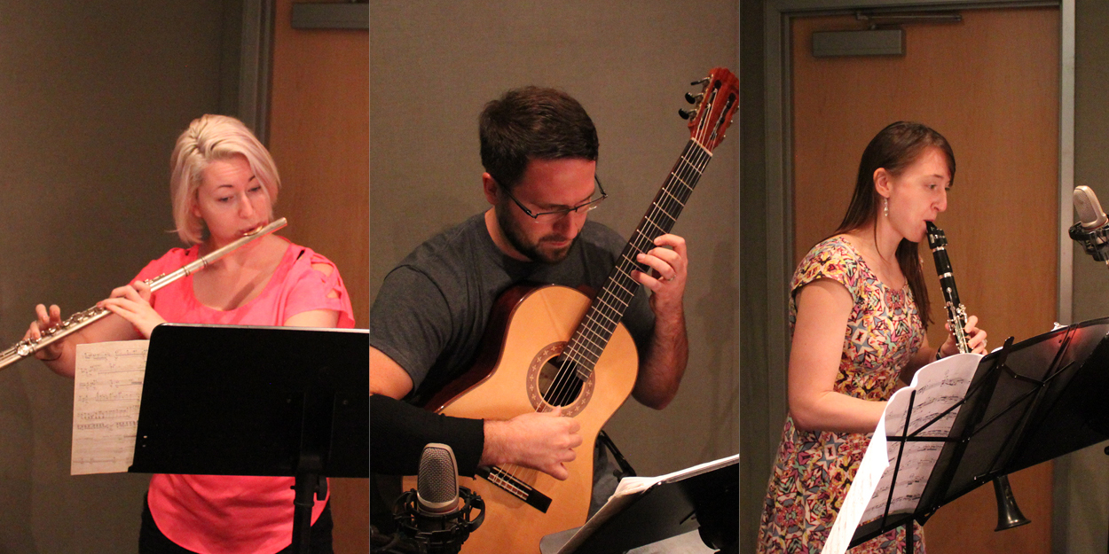 An adult playing flute, an adult playing acoustic guitar, and an adult playing clarinet, all looking at sheet music on music stands in a radio studio
