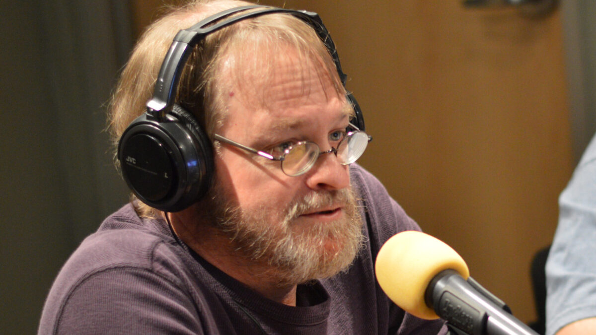 Adult wearing headphones speaking into a microphone in a radio studio