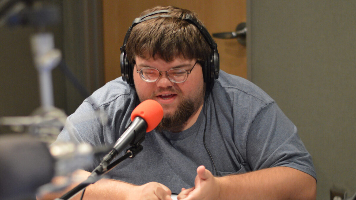 Individual wearing headphones speaking into a microphone and gesturing with their hands in a radio studio