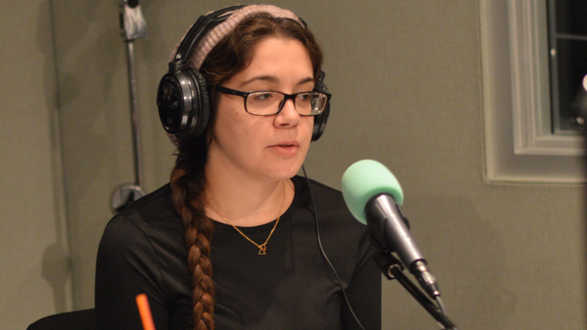 A teen wearing headphones speaking into a microphone in a radio studio