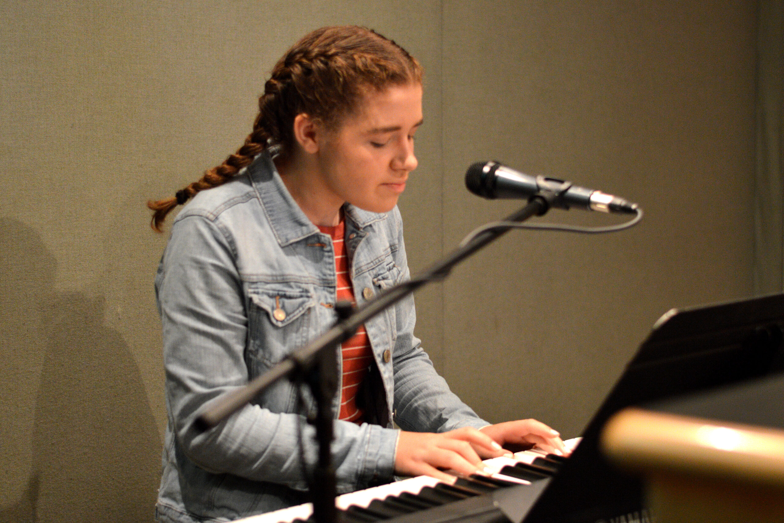 A teen playing piano sitting in front of a microphone and a music stand in a radio studio