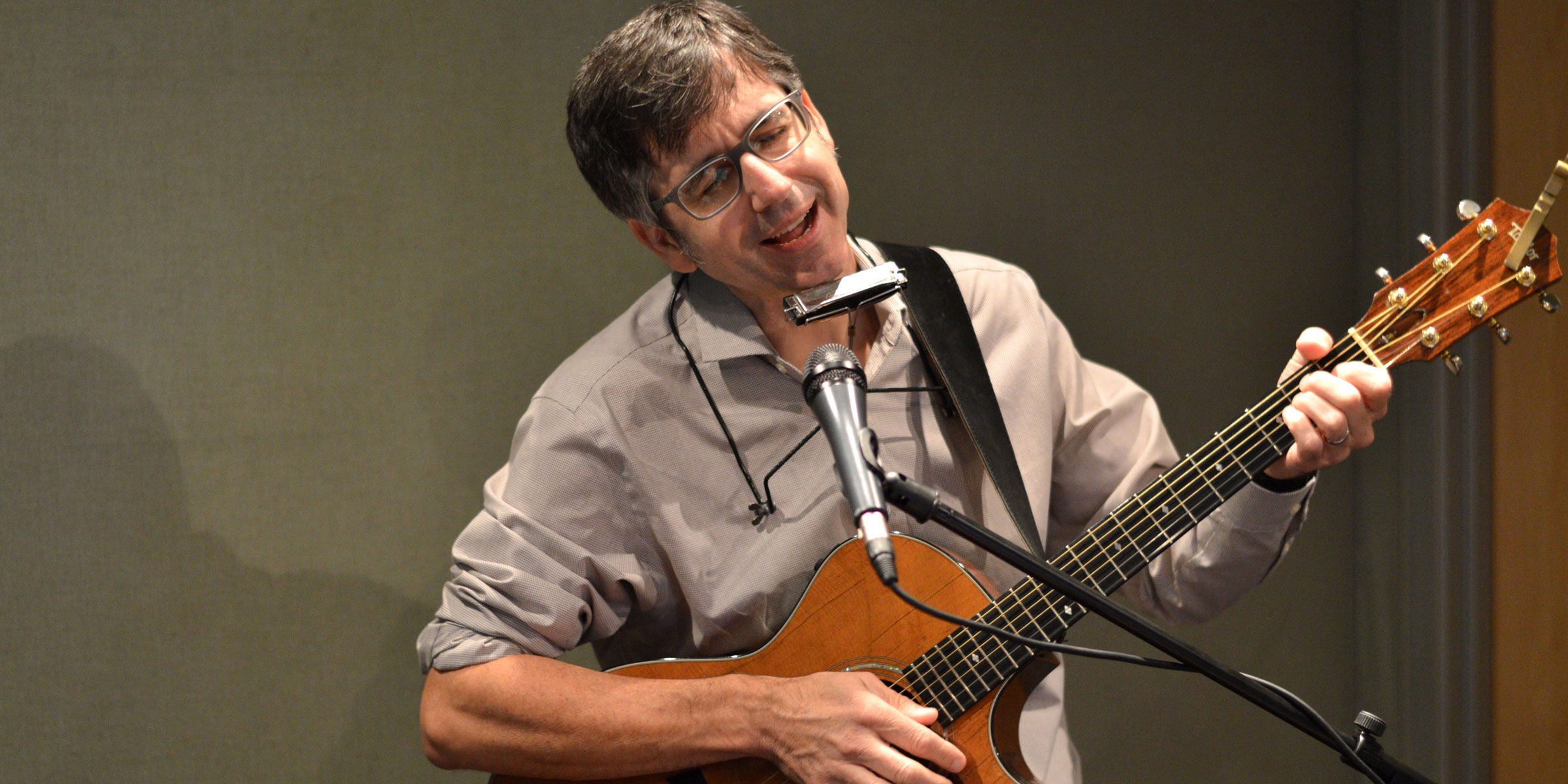 An adult playing guitar and singing into a microphone in a radio studio