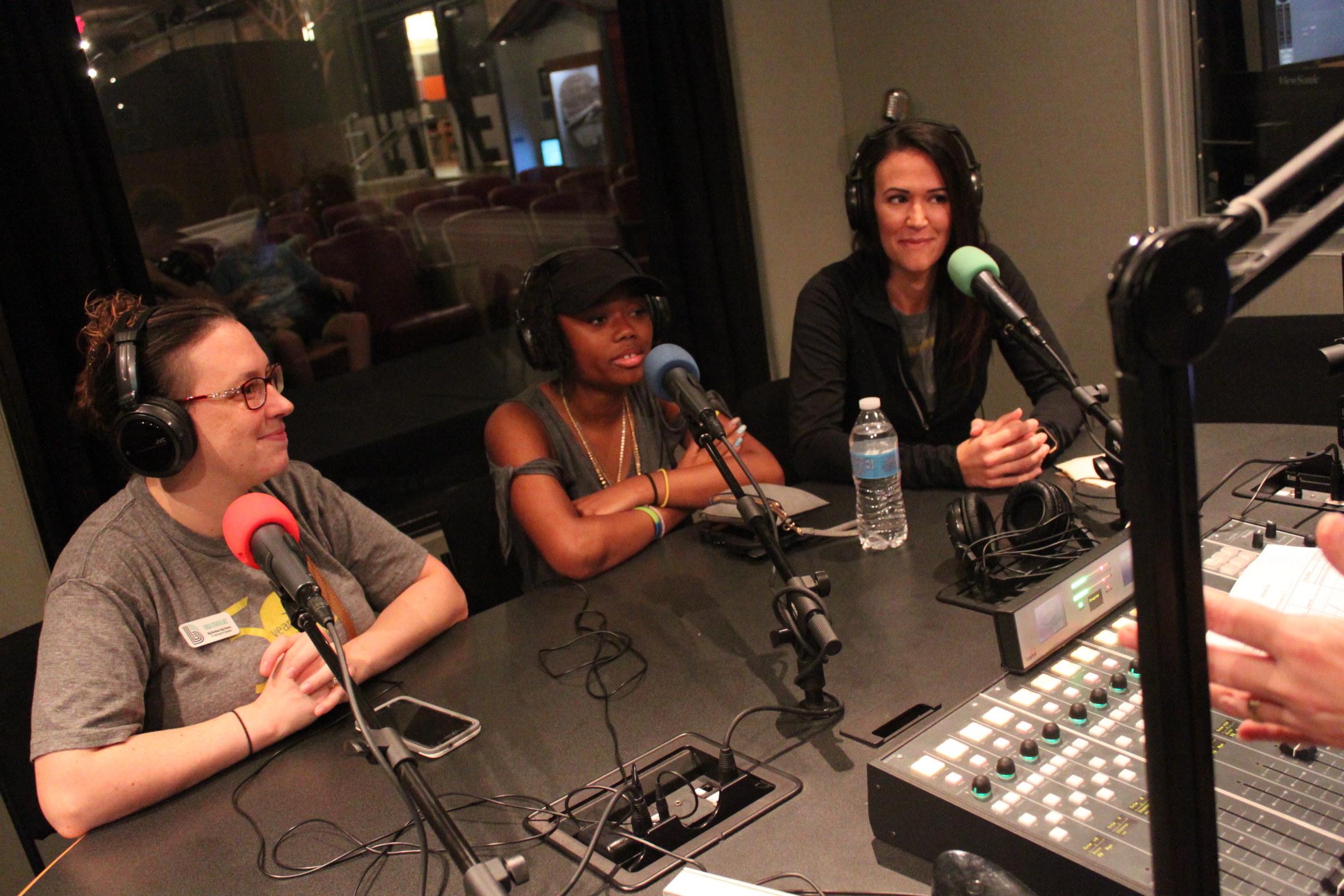 Two adults and one youth wearing headphones speaking into microphones in a radio studio