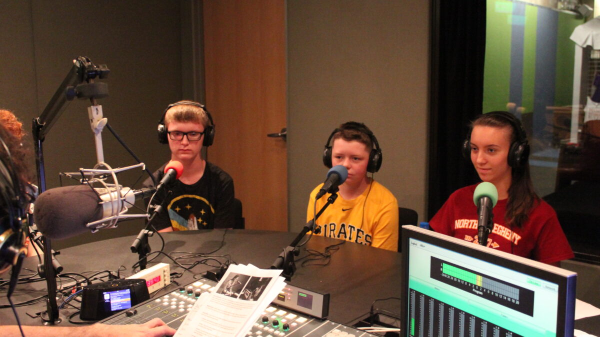 Three youth wearing headphones being interviewed in a radio studio