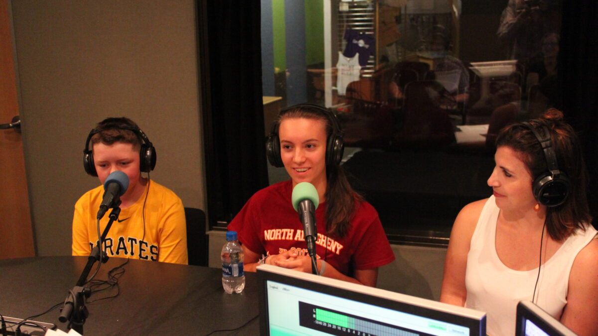 Two youth and one adult wearing headphones and speaking into microphones in a radio studio