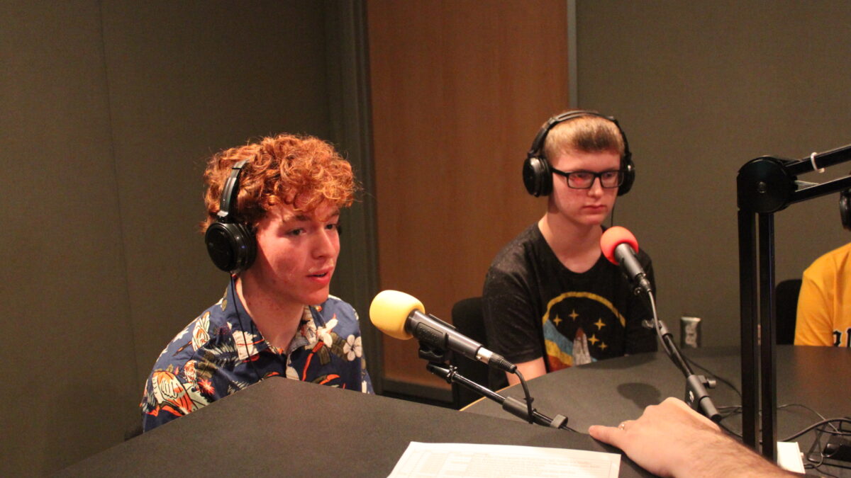 Two teens wearing headphones and speaking into microphones in a radio studio