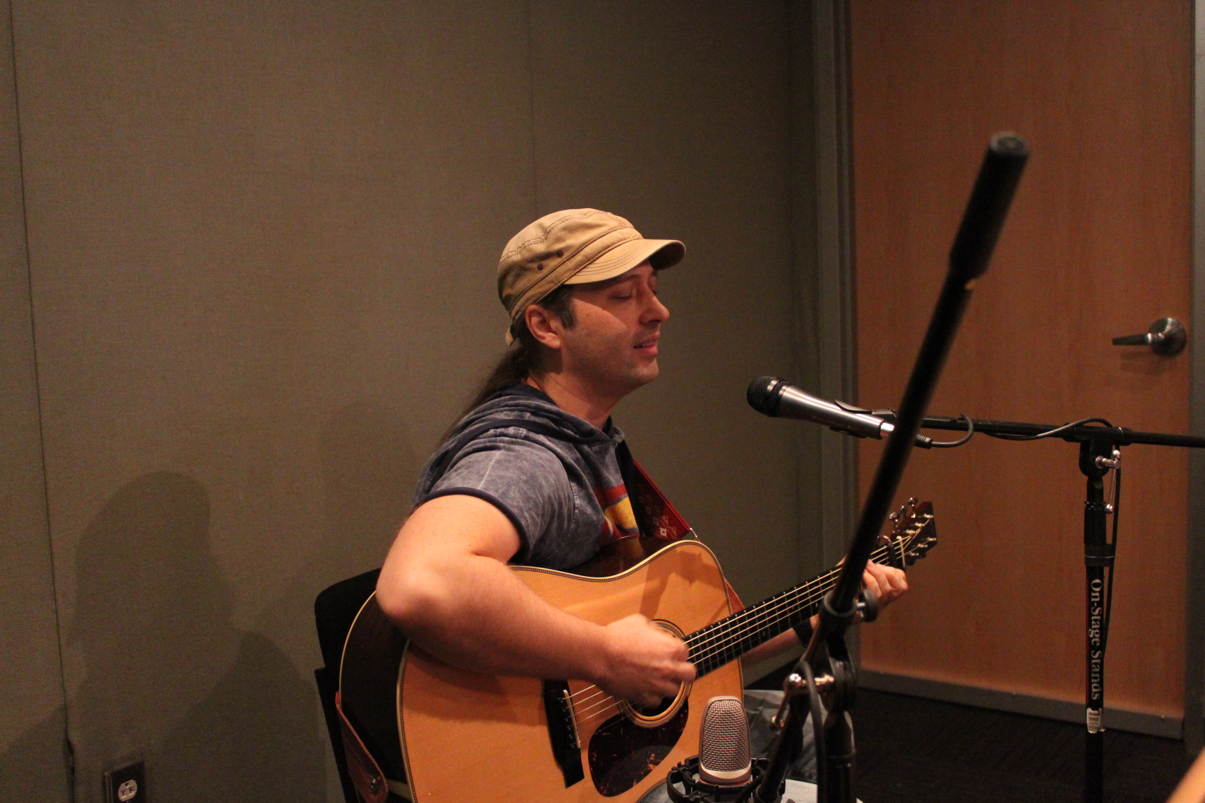 Adult playing guitar and singing into a microphone in a radio studio