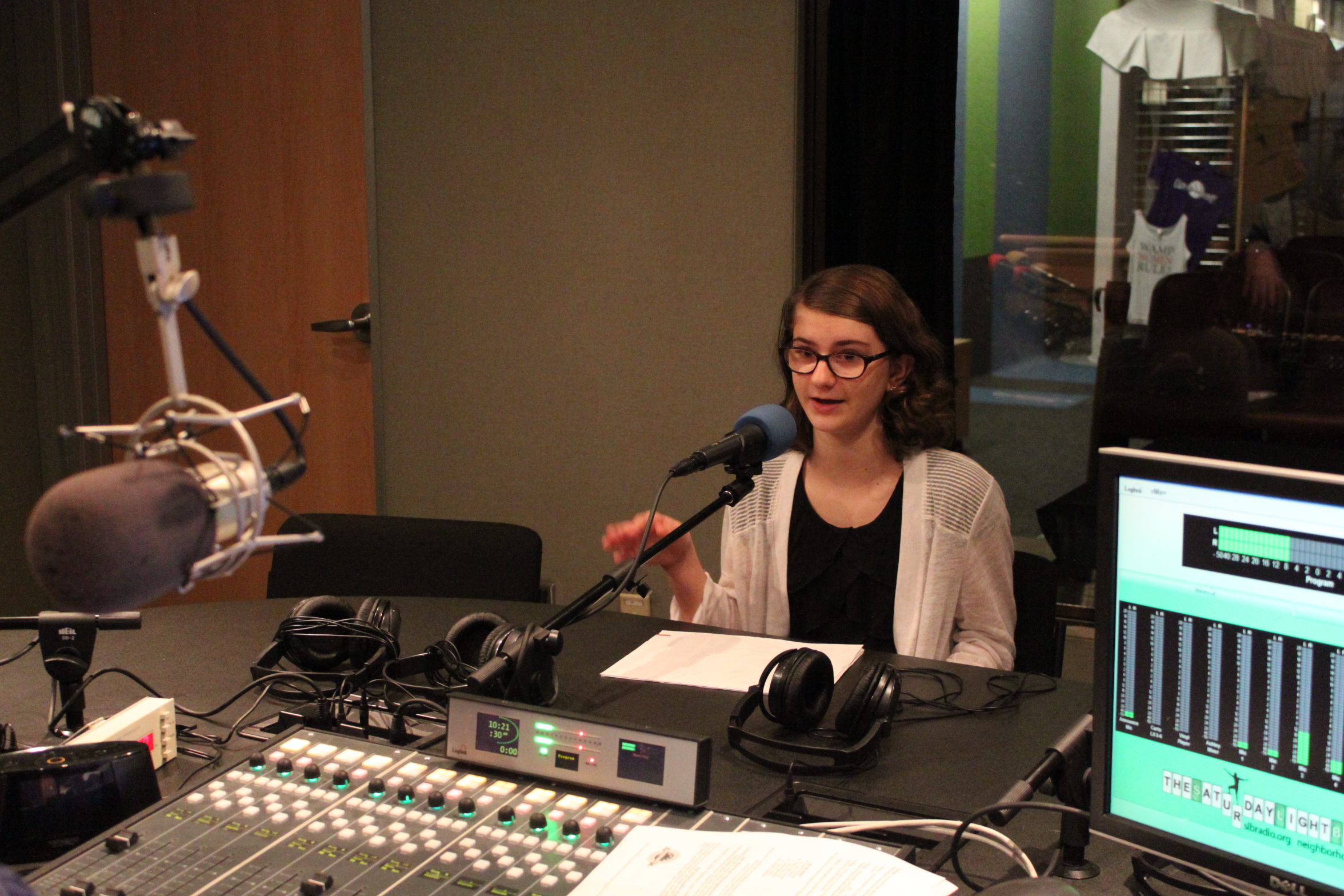 Teen speaking into a microphone and gesturing with their hand in a radio studio