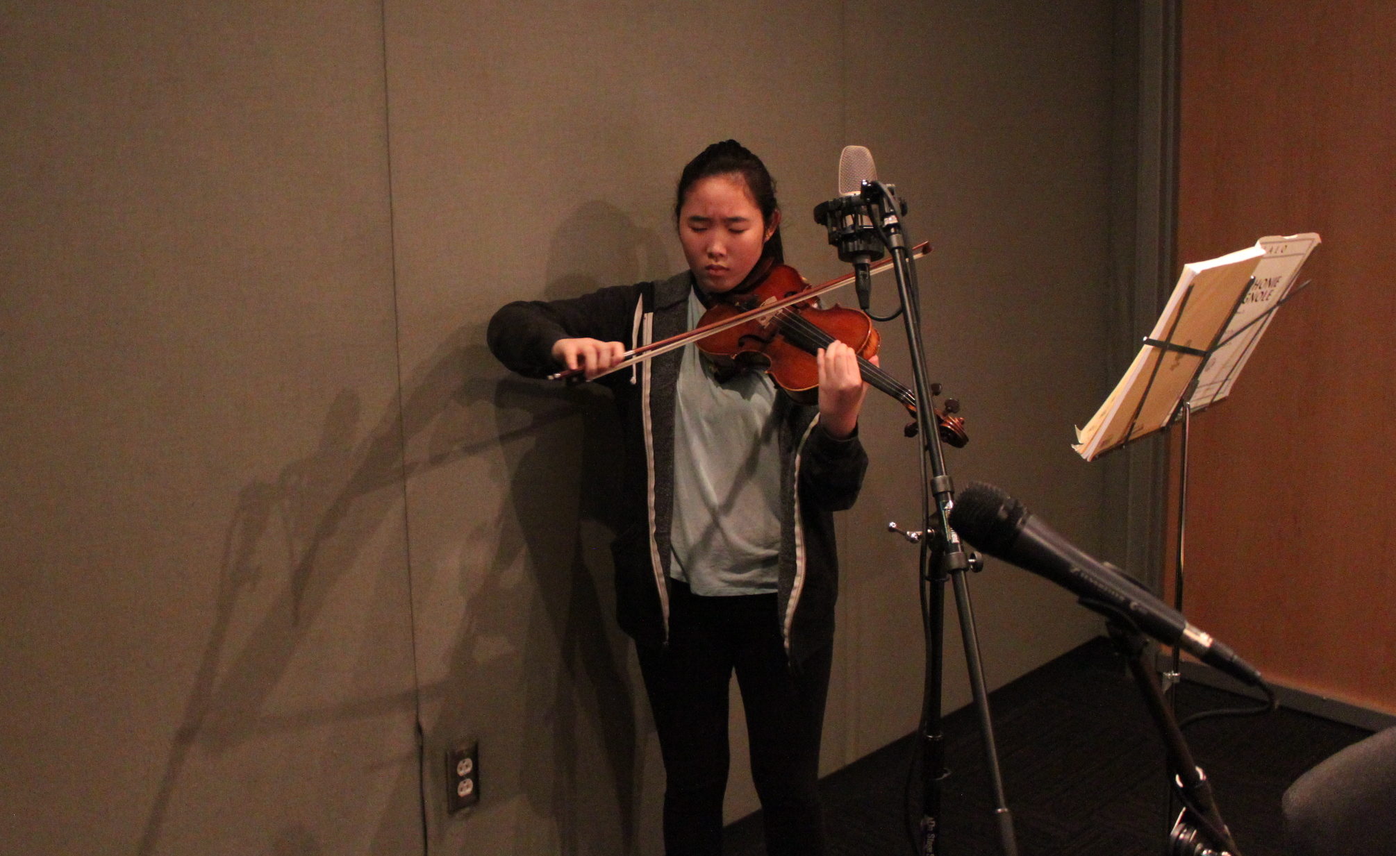 Youth playing violin inf front of sheet music on a music stand in a radio studio