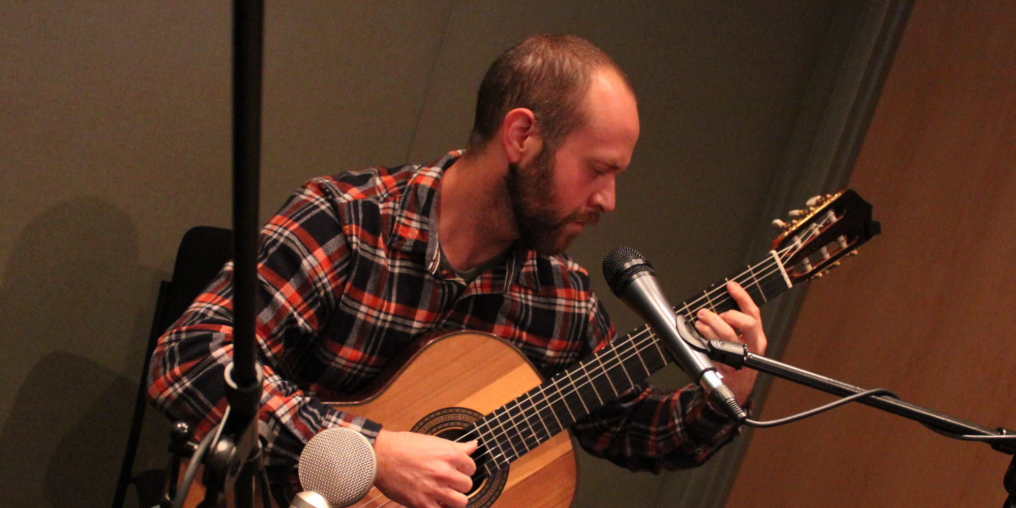 Adult playing guitar and singing into a microphone in a radio studio