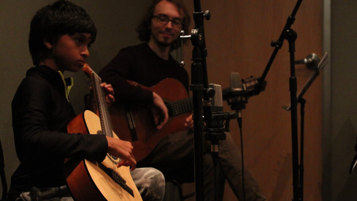 Youth playing guitar and adult holding a guitar in a radio studio