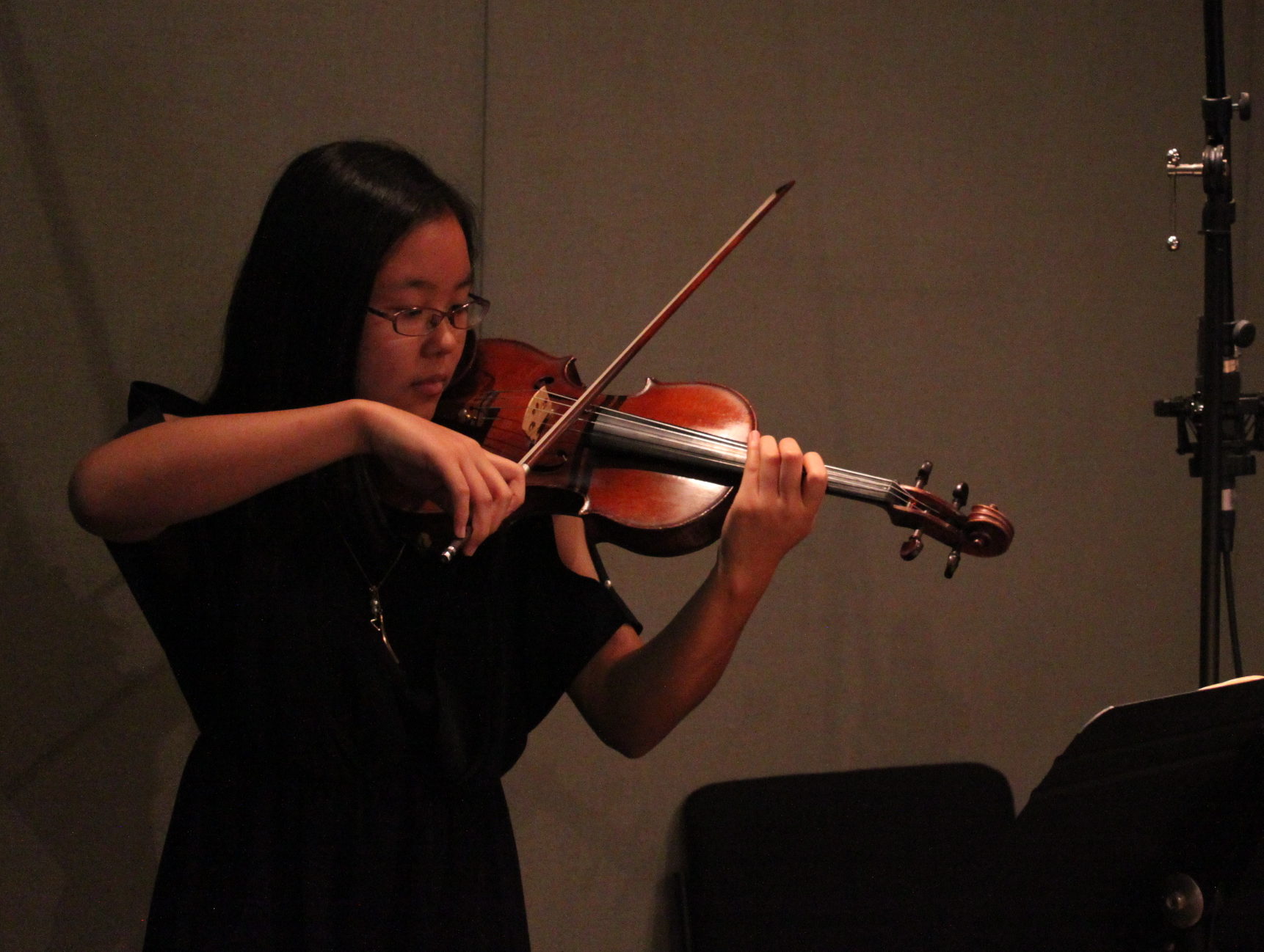 A teen playing violin looking at sheet music on a music stand in a radio studio