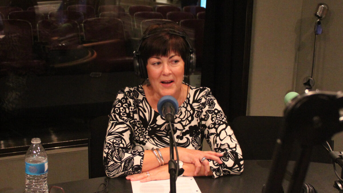 Adult wearing headphones speaking into a microphone in a radio studio