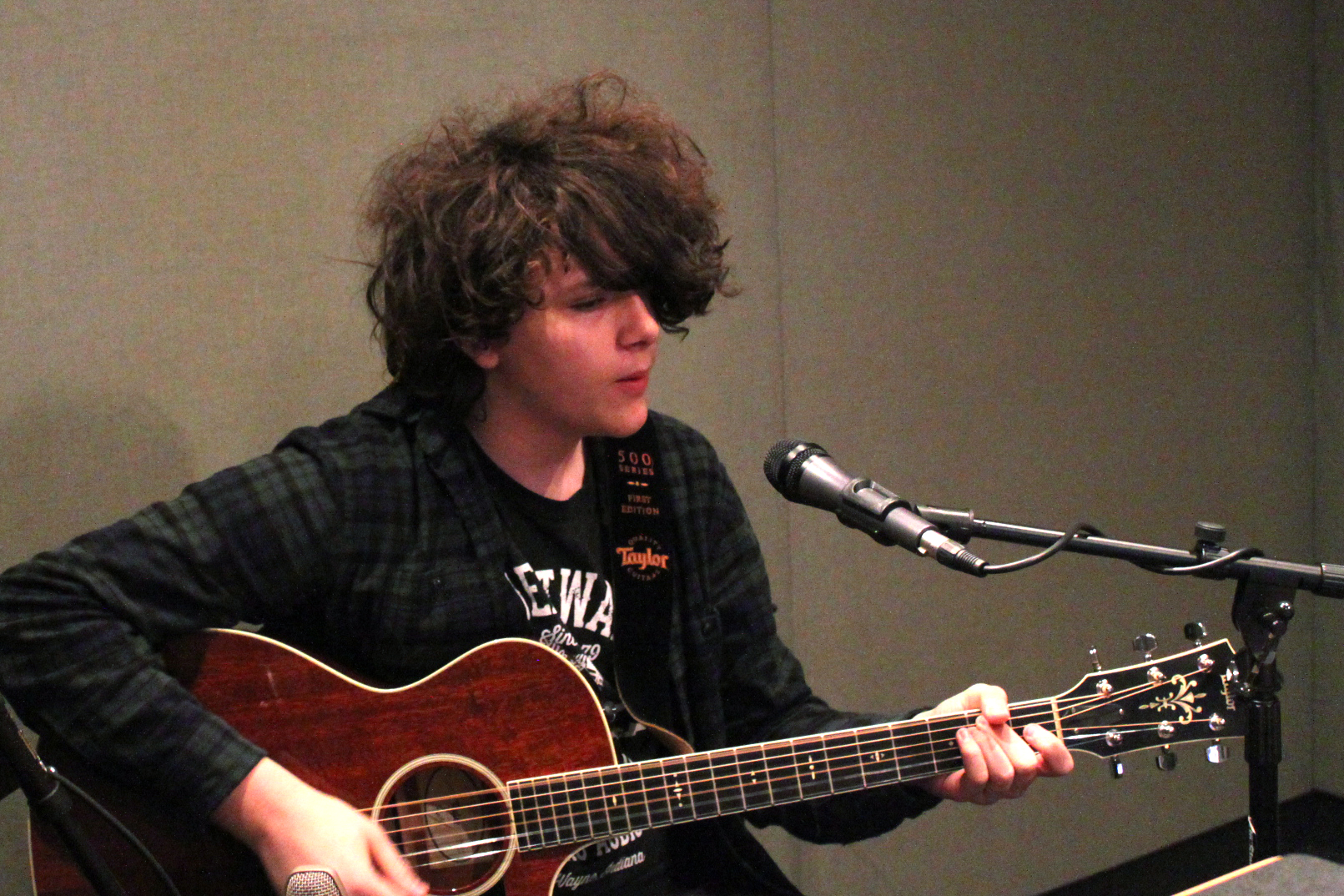 Young individual playing guitar and singing into a microphone in a radio studio