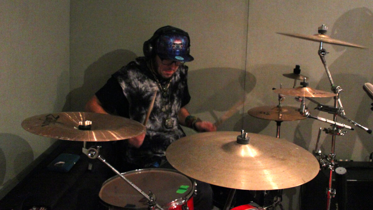 A young adult wearing headphones playing drum set in a radio studio