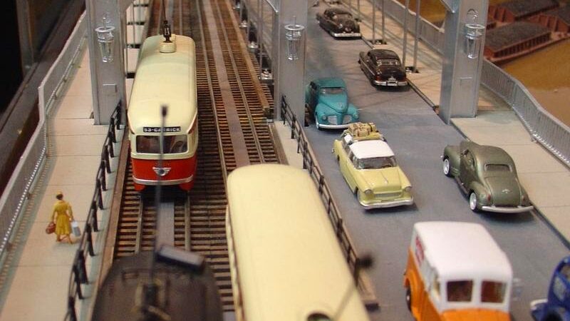 A model set of trains and cars passing under a bridge