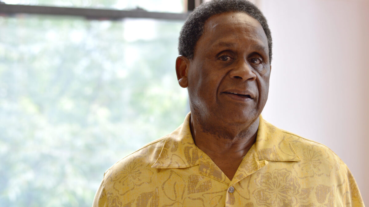 Adult with short black hair and a floral print yellow button up shirt posing in profile