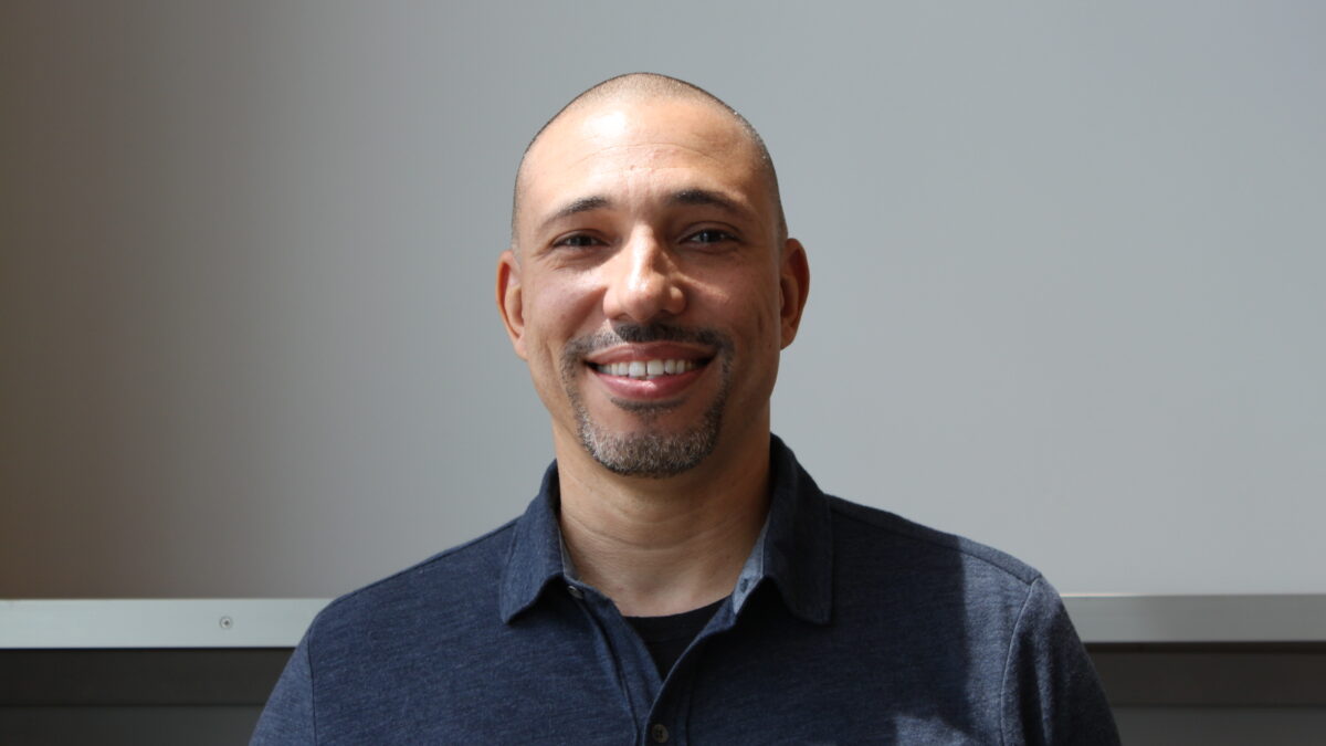 Adult with short black hair and a short graying beard and mustache smiling in profile